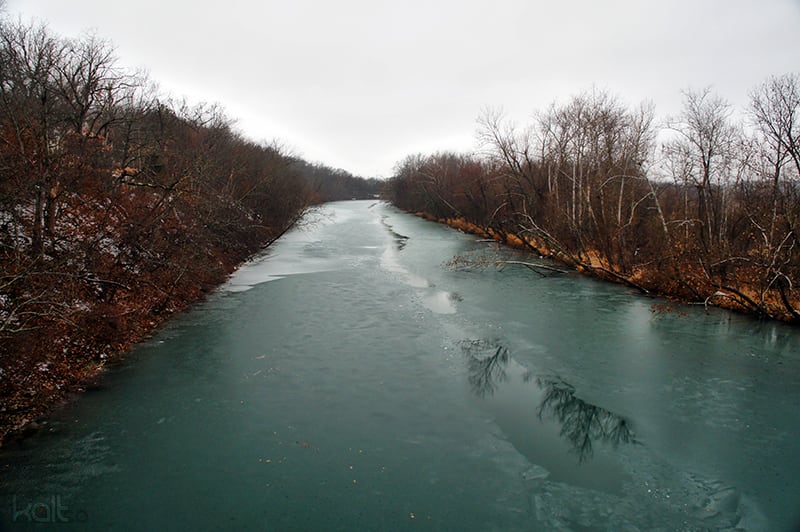 The James River flows past a wooded bank in southwest Missouri with shallow water near the shore.