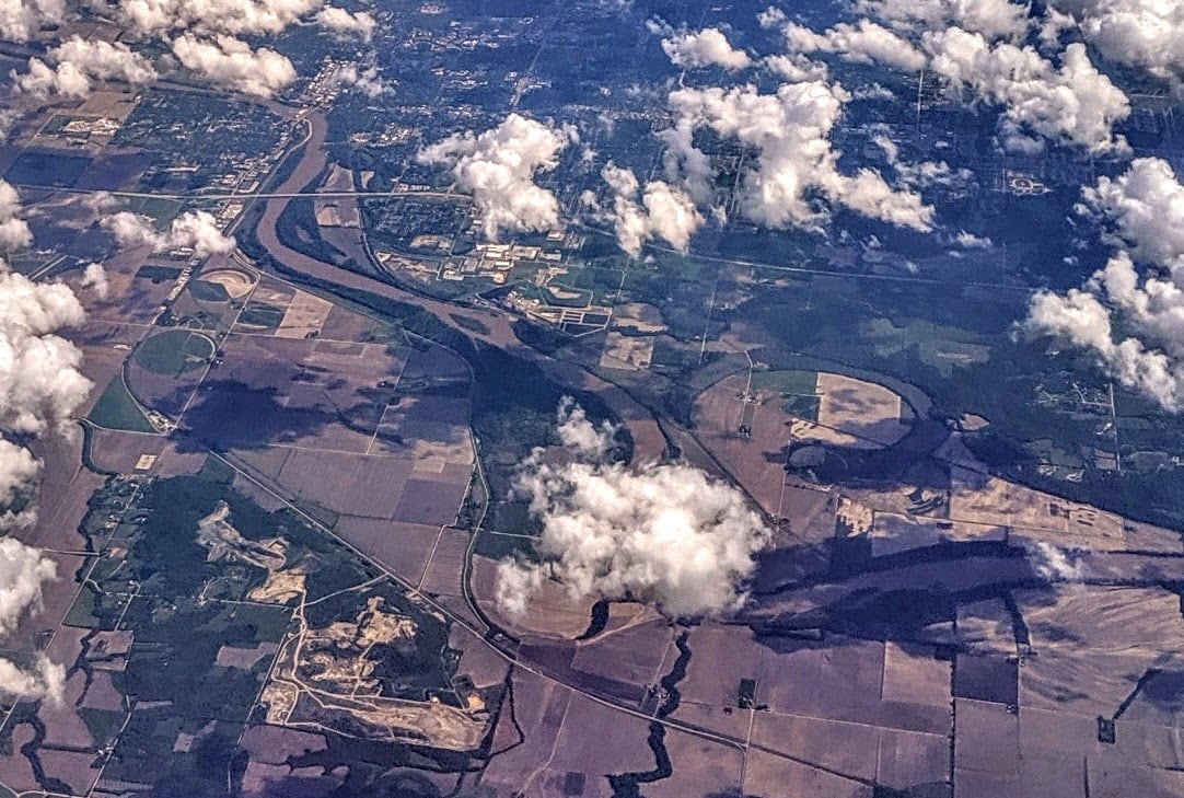 An aerial view shows the Kansas River curving past Lawrence with broad sandbars, wooded banks, and city bridges in the distance.