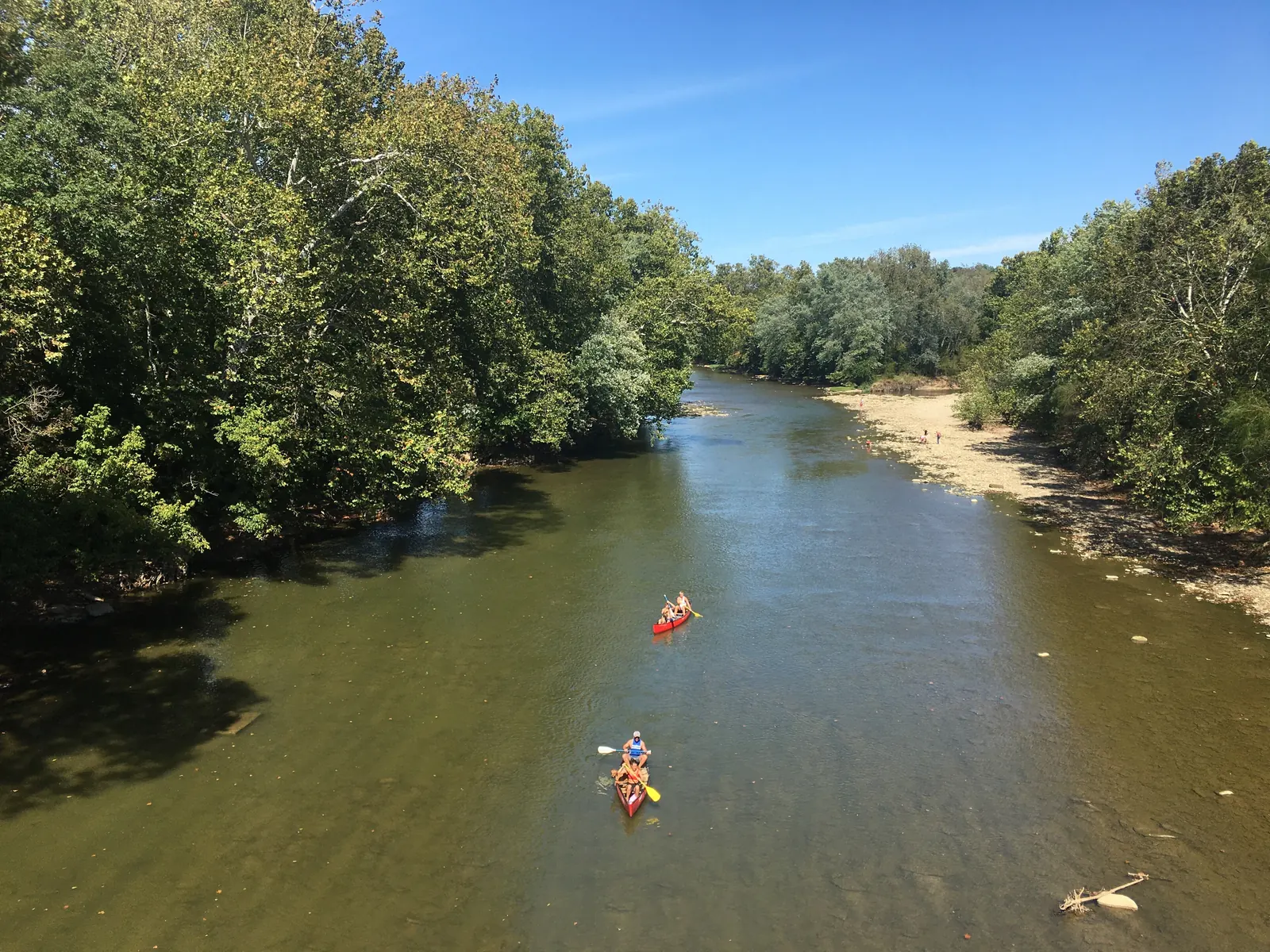 Paddlers move down the Little Miami River near Loveland, Ohio, with wooded banks and a broad gravel bar under clear sky.