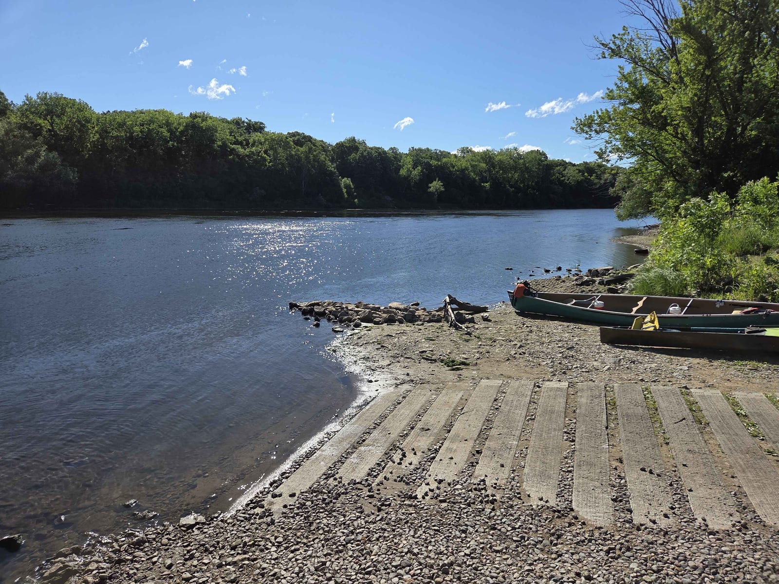 A rocky Mississippi River landing at Norin with canoes pulled up beside the launch and wooded banks across the channel.