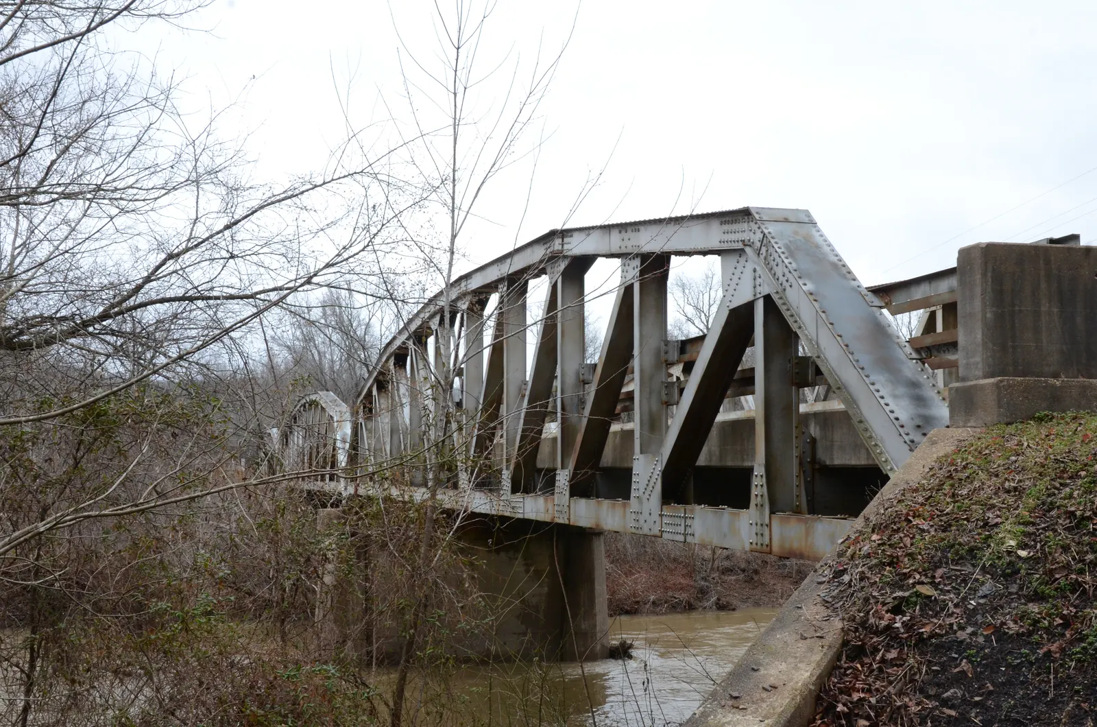 A steel truss bridge crosses the Mulberry River above a rocky channel lined with spring-green trees.