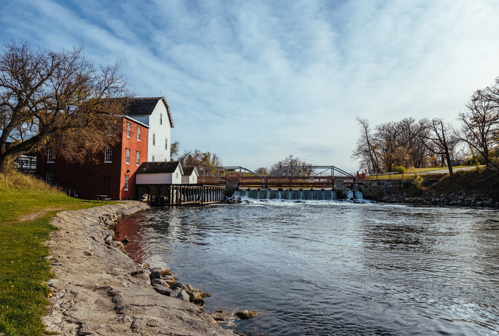 The Otter Tail River flows past the historic Phelps Mill under fall trees.