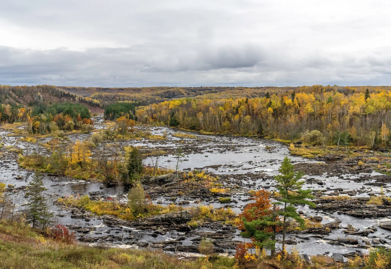 The rocky St. Louis River spreads across a broad valley surrounded by fall foliage in Jay Cooke State Park, Minnesota.