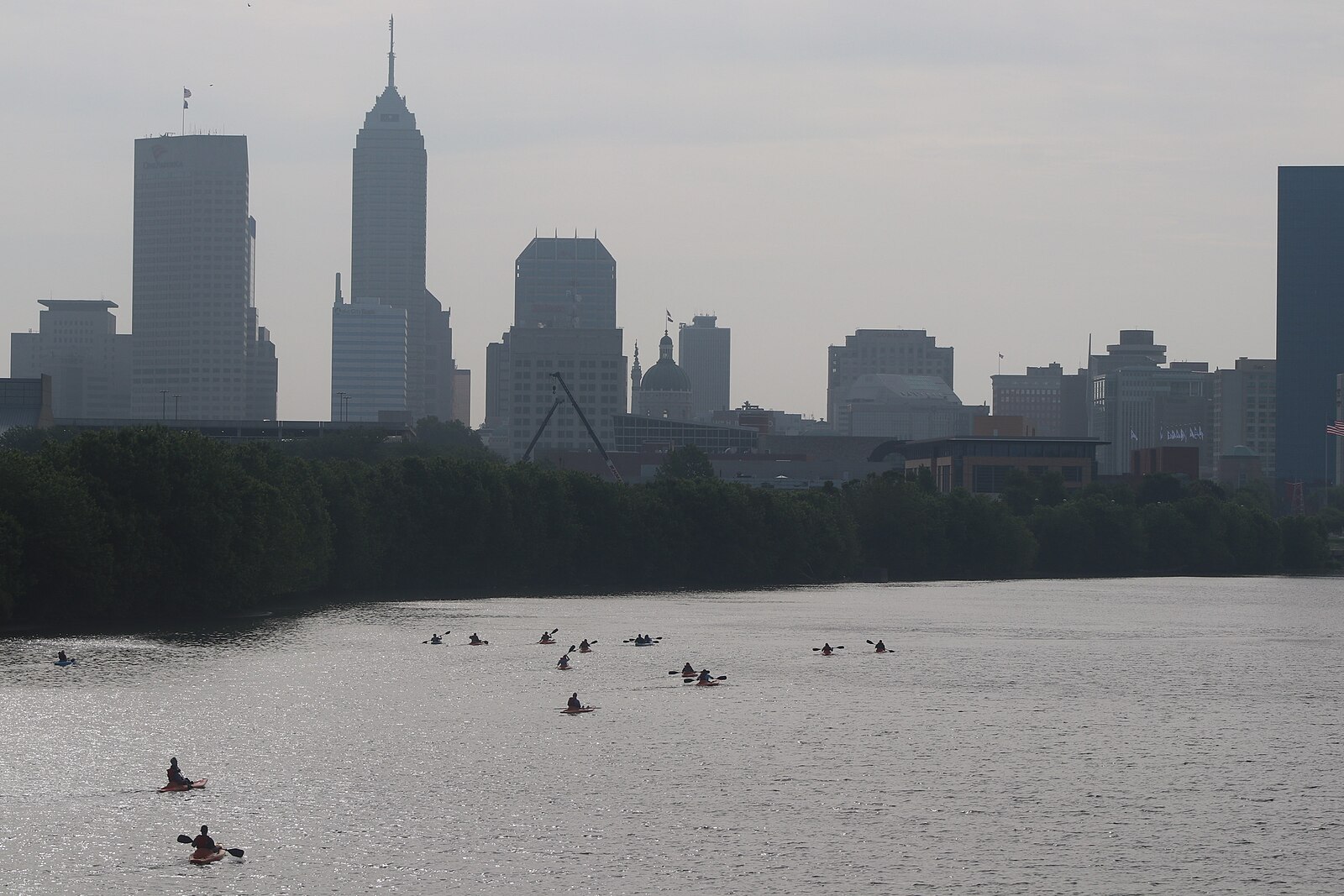 A group of kayakers paddles the White River with the Indianapolis skyline in the distance.