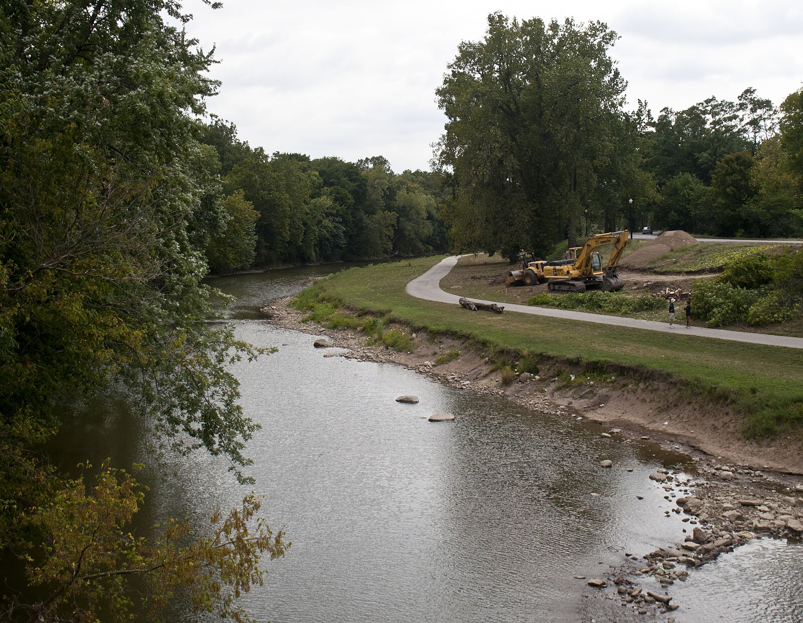 The shallow White River curves past a wooded bank and riverfront trail in Muncie.